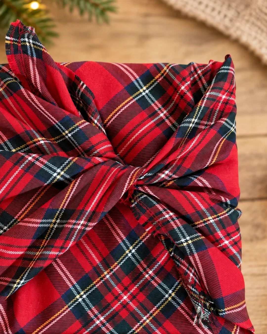 Gros plan du nœud d'un emballage cadeau en tissu tartan rouge, avec sa double couture et sa petite frange naturelle. Emballage réutilisable fait à la main au Québec.
